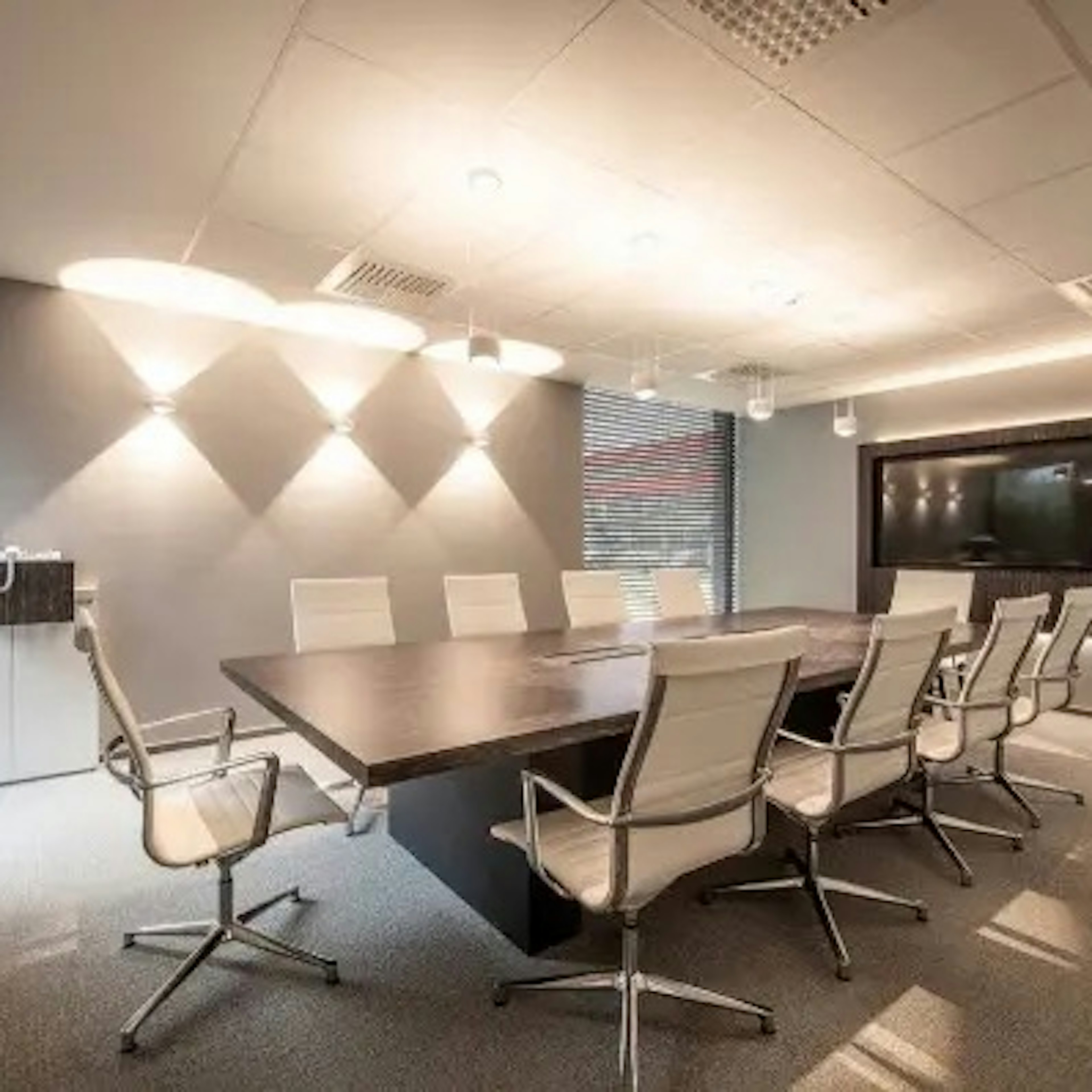 Modern boardroom with a long dark wood conference table surrounded by white leather high-back chairs under warm downlighting.
