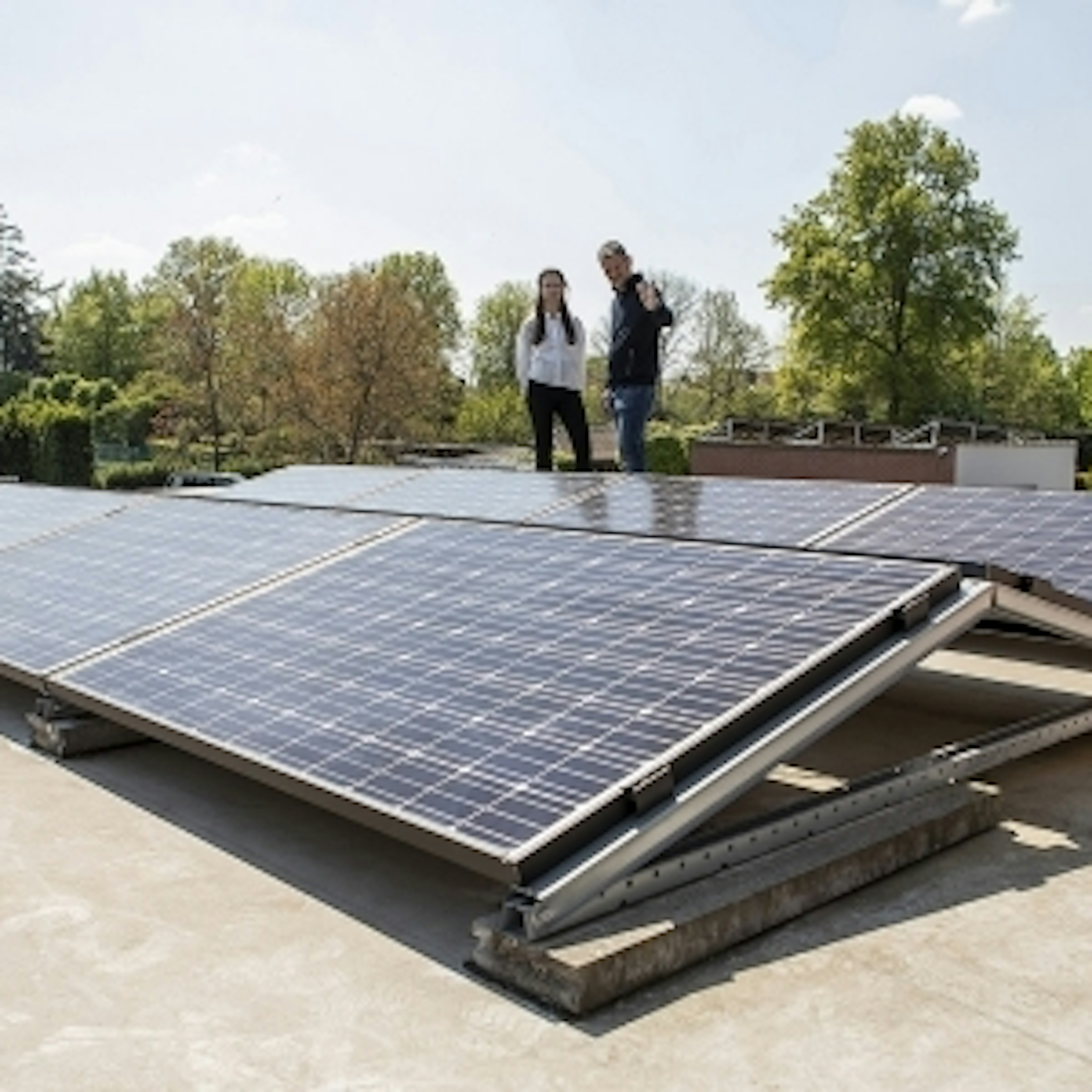 Twee mensen naast zonnepanelen op een plat dak