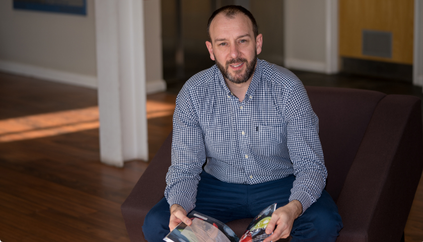 Erudus founder, Jon Shayler, sitting holding a magazine.