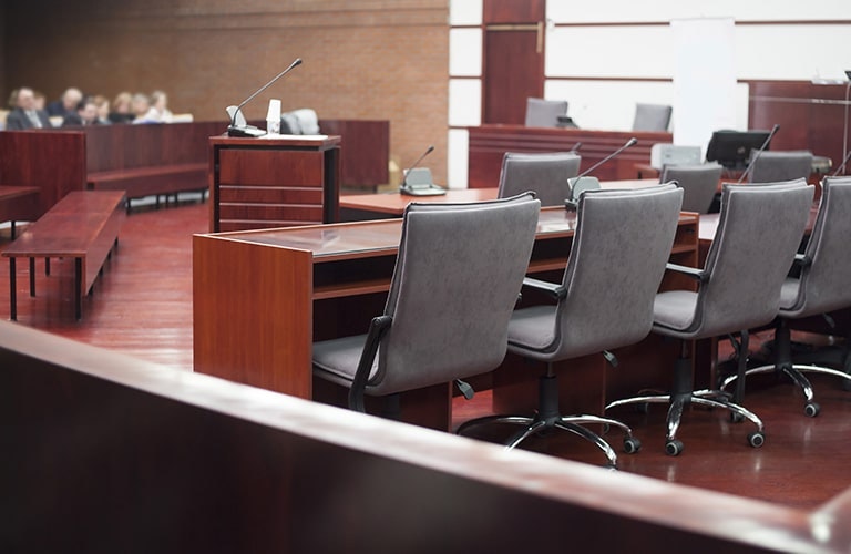 Courtroom with oak wooden tables flooring and grey office chairs with small audience 