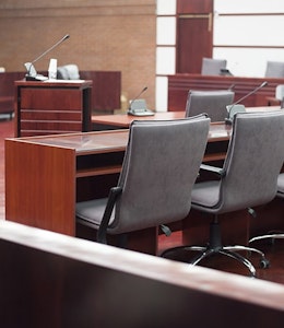 Courtroom with oak wooden tables flooring and grey office chairs with small audience 