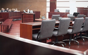 Courtroom with oak wooden tables flooring and grey office chairs with small audience 