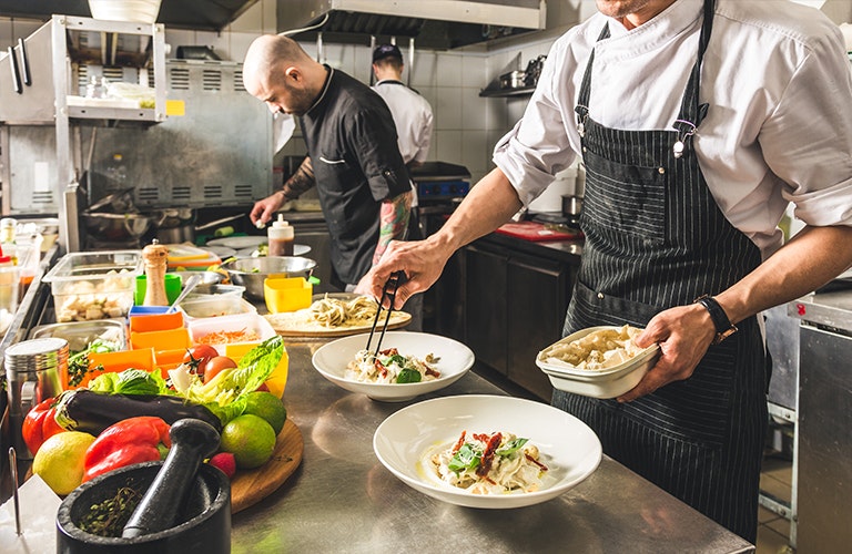 Chef Serving Food in Kitchen Chefs in the kitchen serving food into plates ready to serve