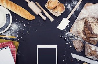 Phone on cooking worktop surrounded by baked goods and notebooks
