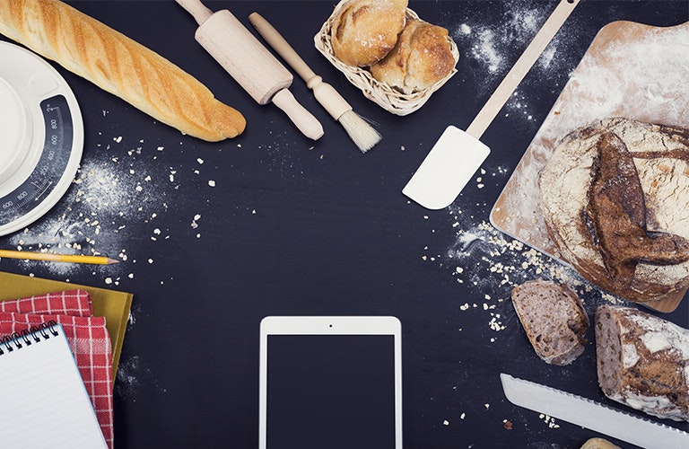 Phone on cooking worktop surrounded by baked goods and notebooks