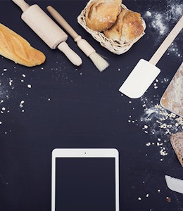 Phone on cooking worktop surrounded by baked goods and notebooks