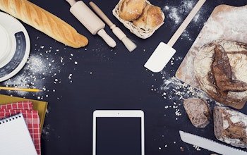 Phone on cooking worktop surrounded by baked goods and notebooks