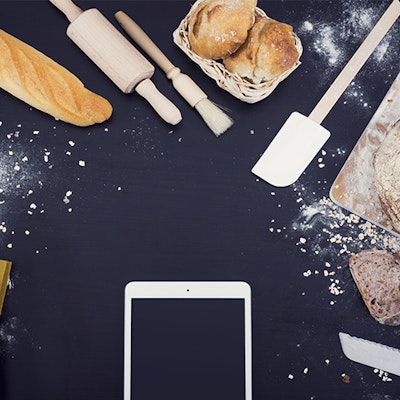 Phone on cooking worktop surrounded by baked goods and notebooks