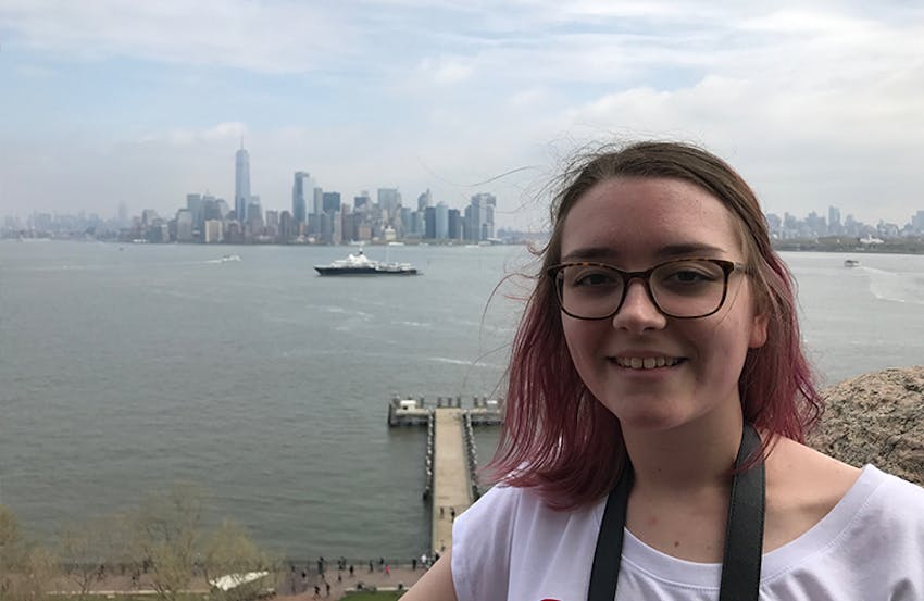 beth newton at the statue of liberty with the nyc skyline in the background 