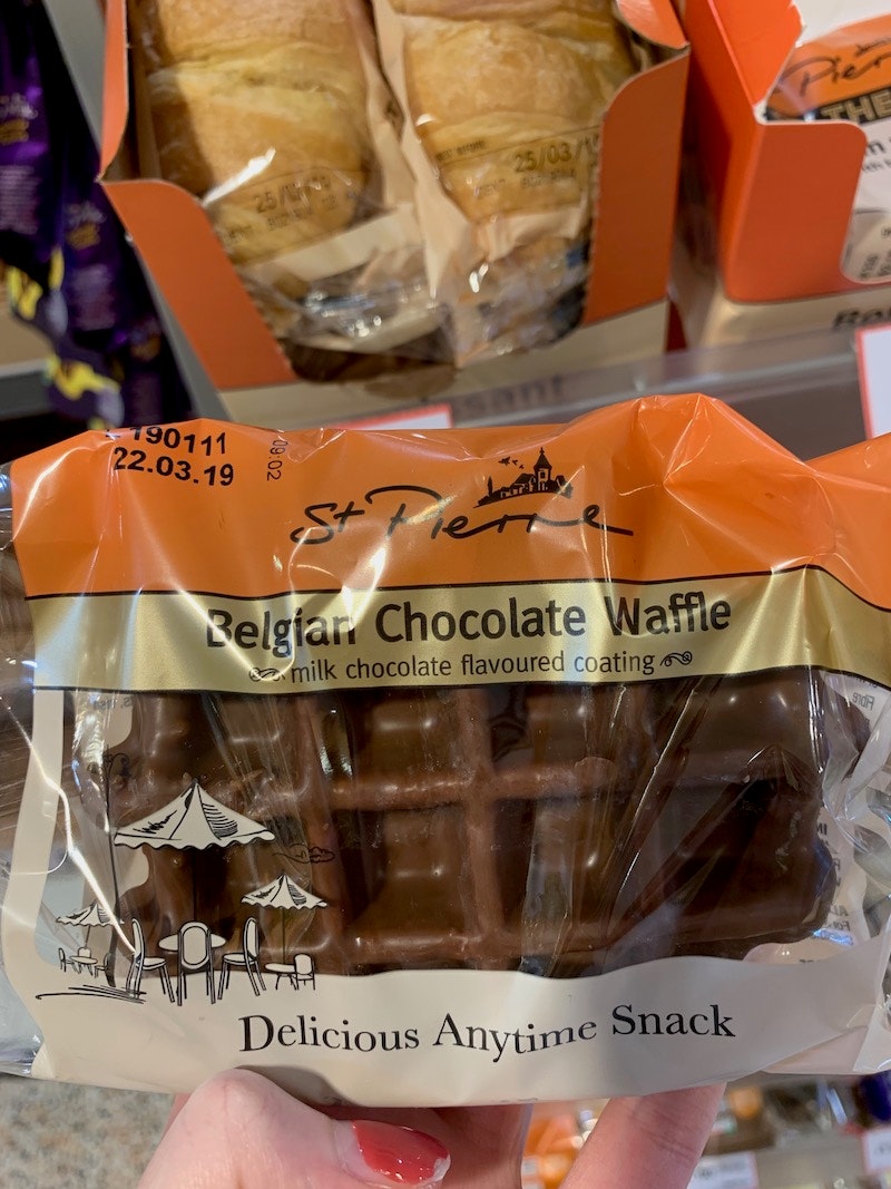 girl holding a square waffle covered in belgian chocolate in packaging in a supermarket aisle 