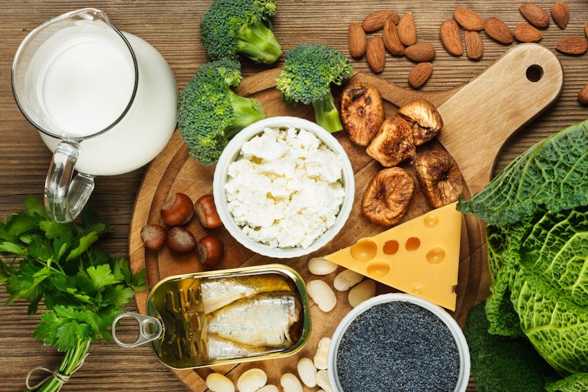 jug of milk on a table with various cheeses, mushrooms, nuts, fish, chia seeds and broccoli on a wooden chopping board 