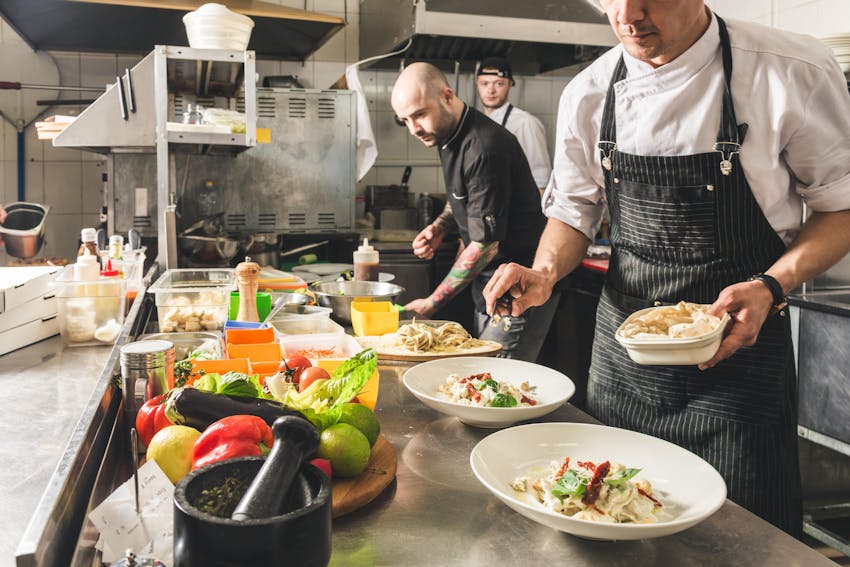 A group of chefs in a restaurant kitchen preparing dishes with lots of different ingredients