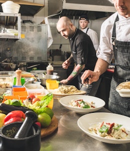 Chefs carefully preparing dishes A group of chefs in a restaurant kitchen preparing dishes with lots of different ingredients