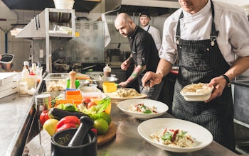 Chefs carefully preparing dishes A group of chefs in a restaurant kitchen preparing dishes with lots of different ingredients