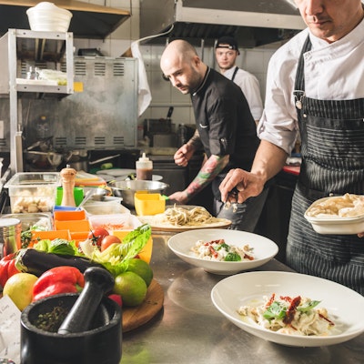 A group of chefs in a restaurant kitchen preparing dishes with lots of different ingredients