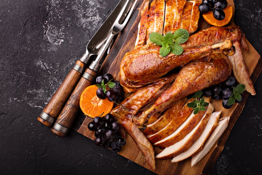 crispy cooked turkey sliced and garnished with grapes and orange on a wooden chopping board 