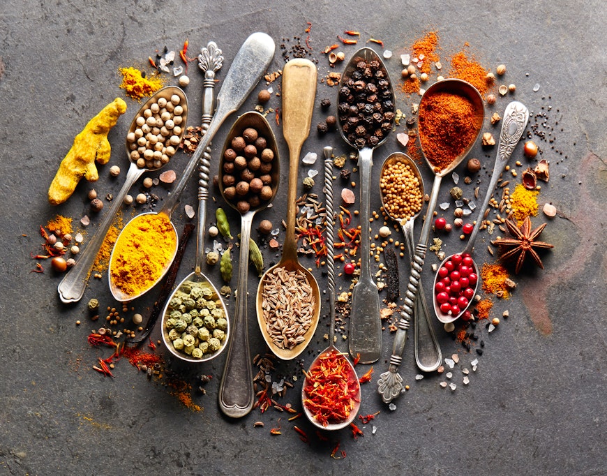 a colourful array of herbs and spices on various gold and silver brass spoons