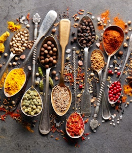 a colourful array of herbs and spices on various gold and silver brass spoons