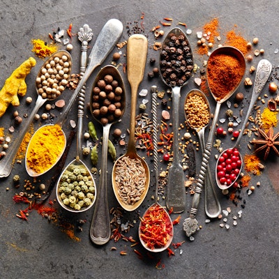 a colourful array of herbs and spices on various gold and silver brass spoons