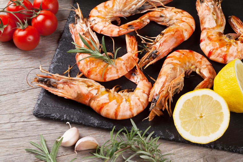 shrimp on a black display board with sliced lemon cherry tomatoes and garlic 