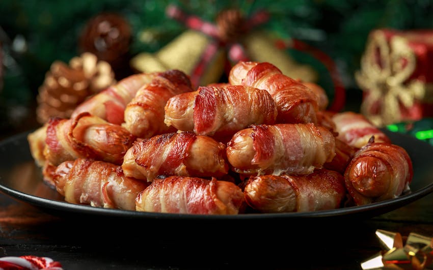 a black plate piled with cocktail sausages wrapped in bacon 