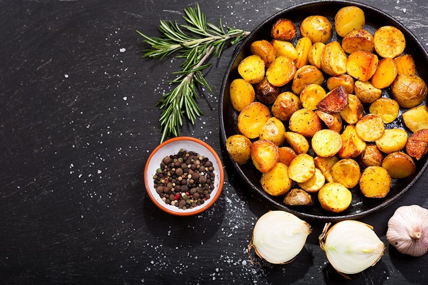 a bowl of crispy roast potatoes with a side dish of peppercorns, onions and a garlic bulb 