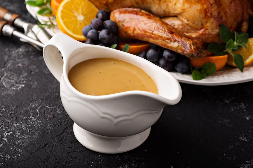 a white china gravy boat filled with gravy in front of a roasted turkey 