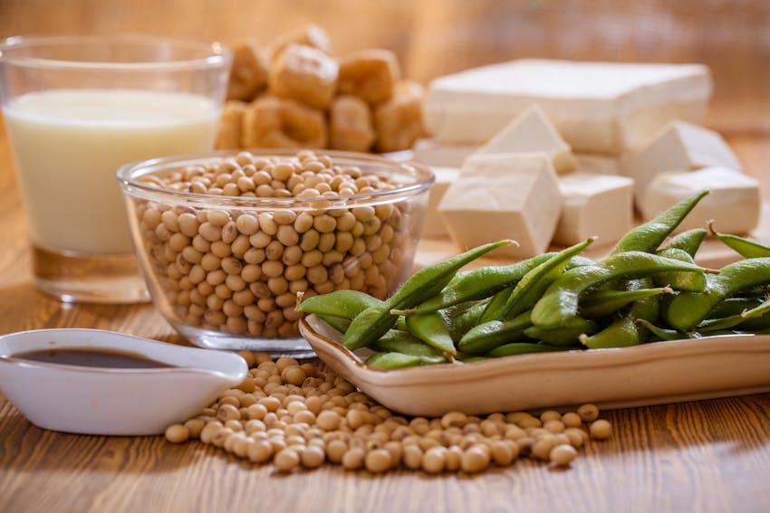 a large clear bowl of soya beans behind a tray of edamame beans, soy sauce and a glass of soya milk 