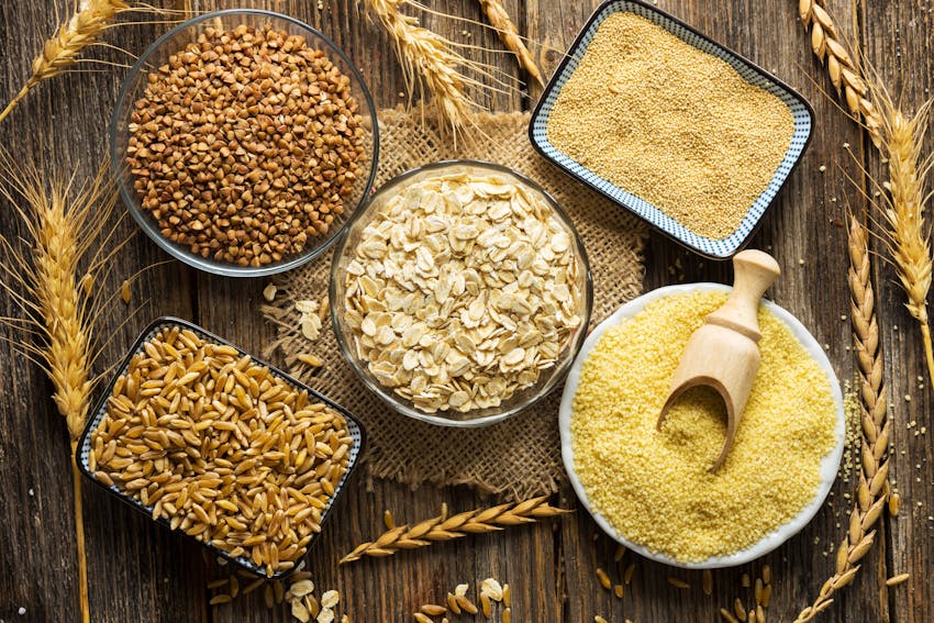 five different bowls of cereals containing gluten on a wooden table surrounded by wheat stalks 