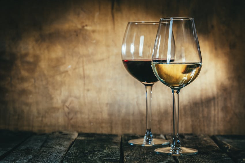 two glasses of wine, one white and one red on a rustic table near a wooden rustic wall 