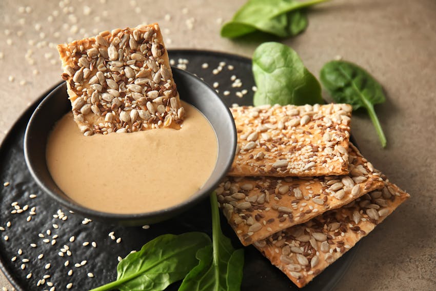 crispy sesame toasts on a black plate dipped in sesame sauce 