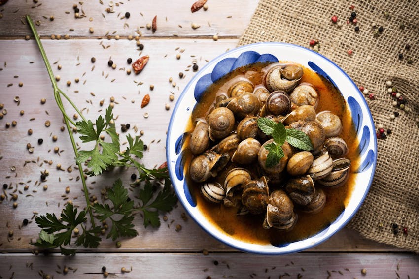 a small plate of l'escargot in sauce topped with fresh leaves