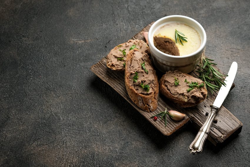 a small wooden chopping board with three slices of crusty bread topped with pate and fresh herbs 