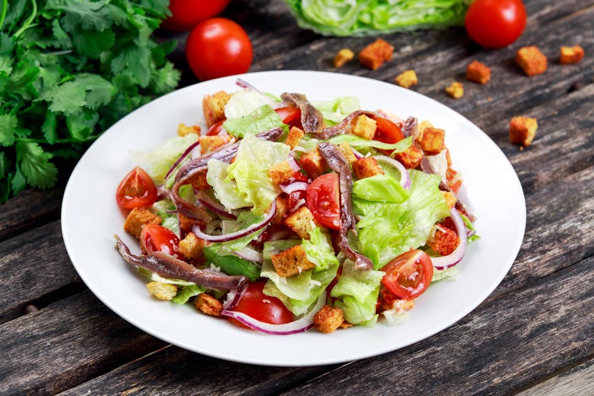 a white dish filled with fresh crispy iceberg lettuce, tomatoes, onions and croutons  