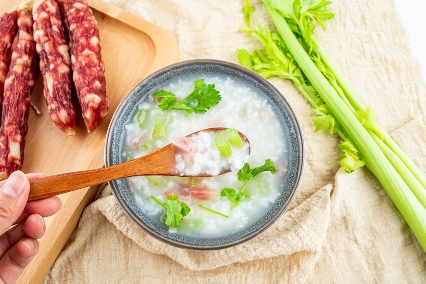 a grey ceramic bowl filled with soup topped with celery next to a wooden chopping board of chorizo and celery sticks 