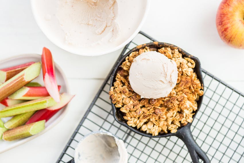 a small cast iron filled with a baked apple crumble topped with a scoop of creamy vanilla ice cream 