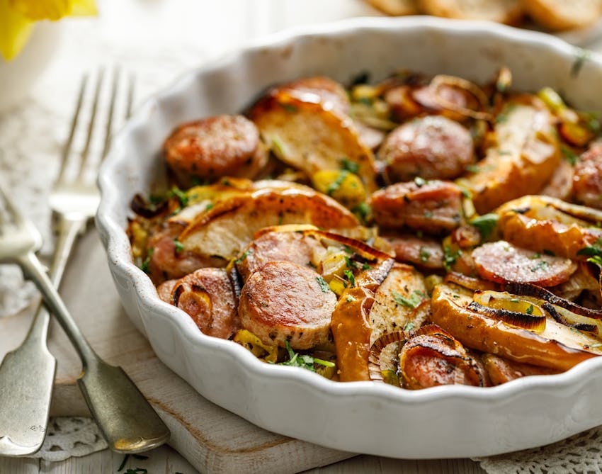 white serving dish filled with cider, apple and sausage casserole topped with herbs 