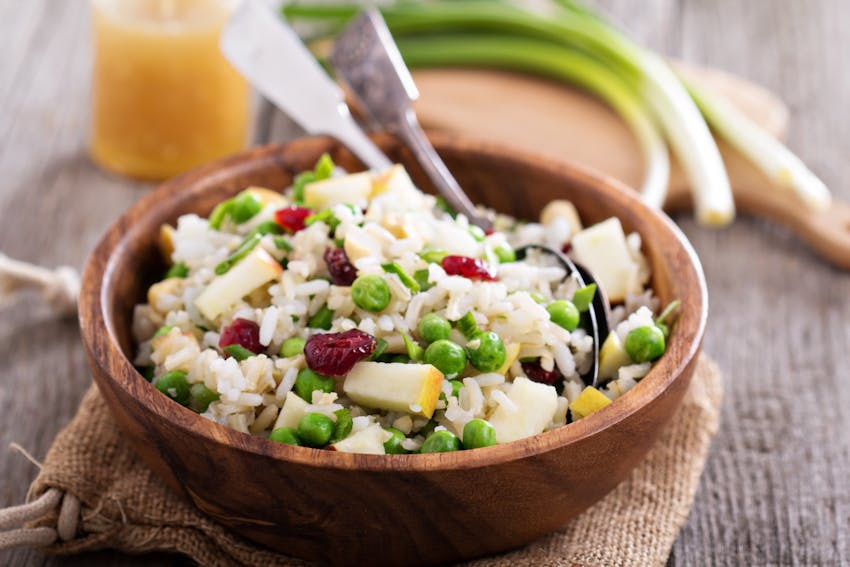 a wooden bowl filled with chorizo, rice, pea and apple salad 