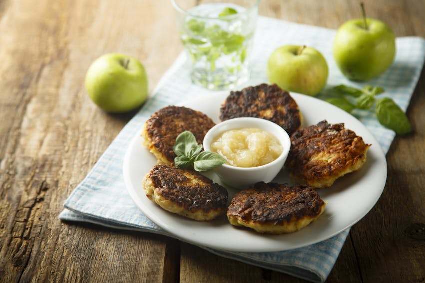 a small white plate with tahini lemon drizzle in the centre with 5 latkes around the tahini 