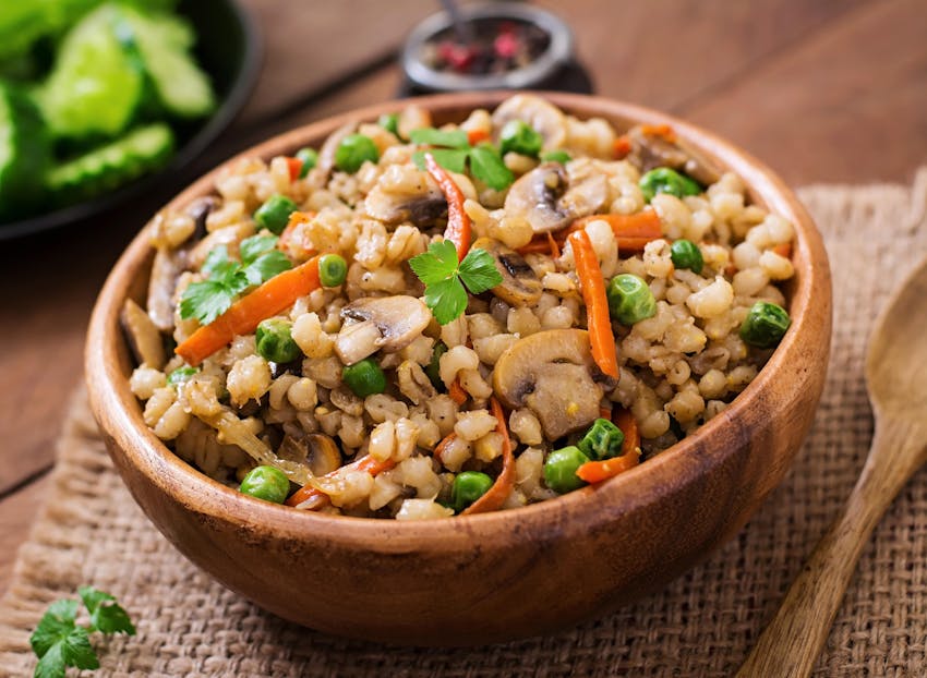 a wooden bowl filled with various grains with peas carrots and mushrooms next to a wooden spoon 