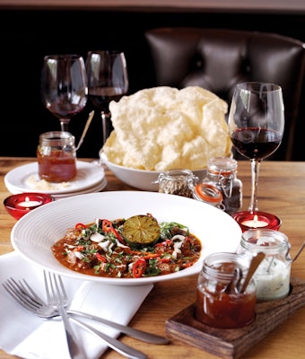 dish of welsh lamb curry served on a table with two small glass jars of condiments a bowl of poppadoms and three glasses or red wine 