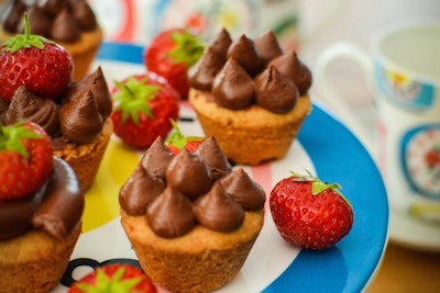 five chocolate mousse and caramel shortbread cups on a blue plate with red strawberries 