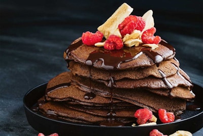 a stack of seven gluten free chocolate pancakes drizzled with chocolate sauce and raspberries 