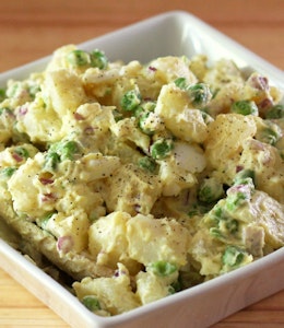 square white dish filled with a creamy potato, bacon and pea salad 