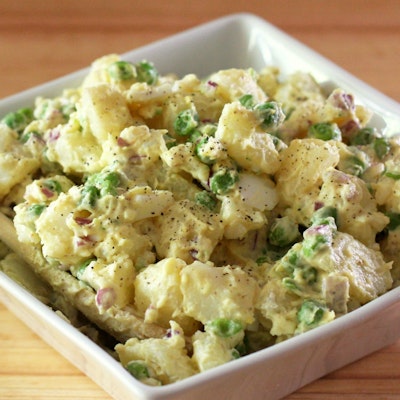 square white dish filled with a creamy potato, bacon and pea salad 