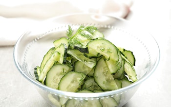 a clear glass bowl filled with green cucumber and dill salad 