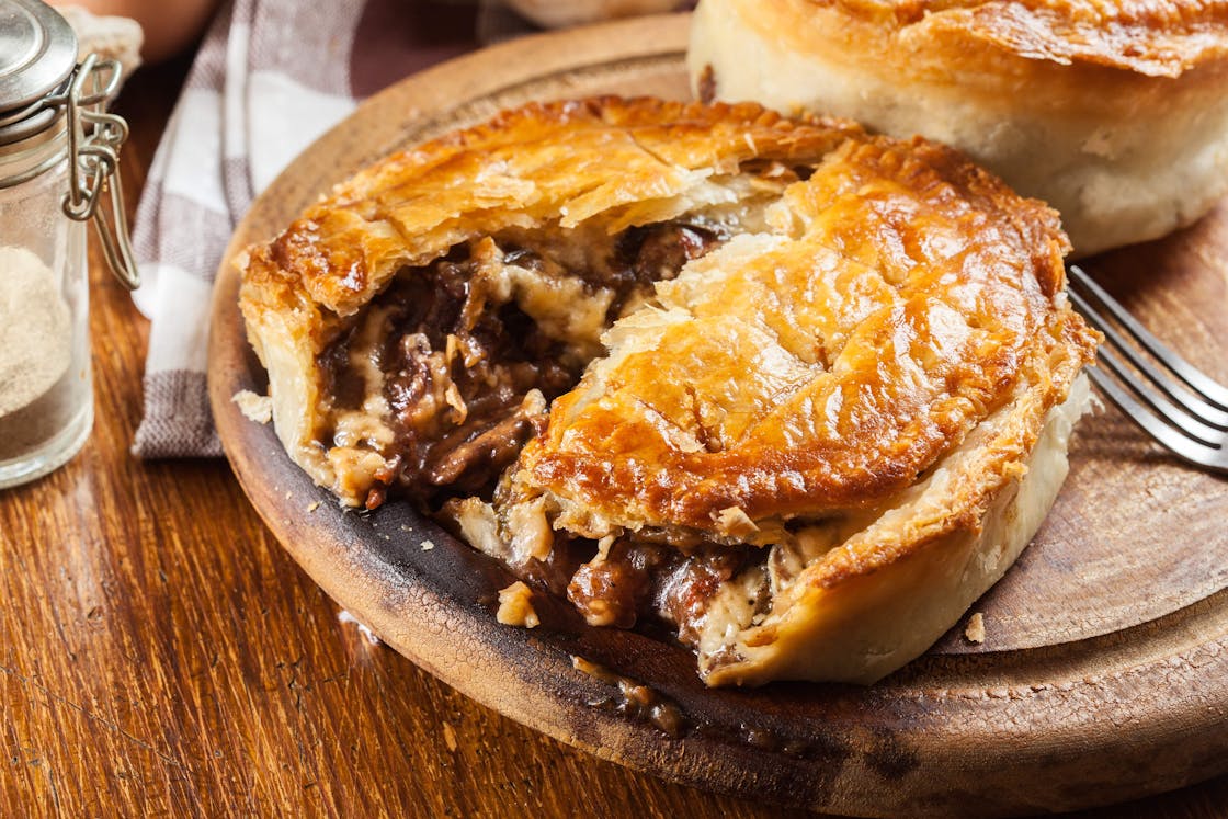 Beef & Stilton Pie pie baked in a brown dish 1/3 cut open and revealing beef and stilton meat and gravy filling