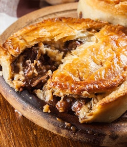 Beef & Stilton Pie  pie baked in a brown dish 1/3 cut open and revealing beef and stilton meat and gravy filling