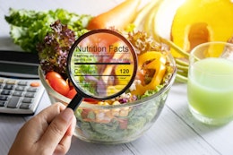 hand holding a magnifying glass illuminates nutrition and calorie information infront of a bowl of fresh crispy salad next to a calculator 