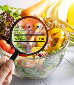 The government are set to introduce Mandatory Calorie Labelling  hand holding a magnifying glass illuminates nutrition and calorie information infront of a bowl of fresh crispy salad next to a calculator